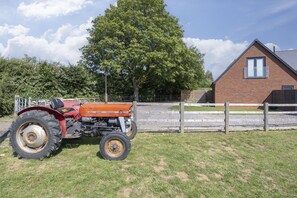 A tractor parked in a grassy area with a brick building and a wooden fence in the background.
