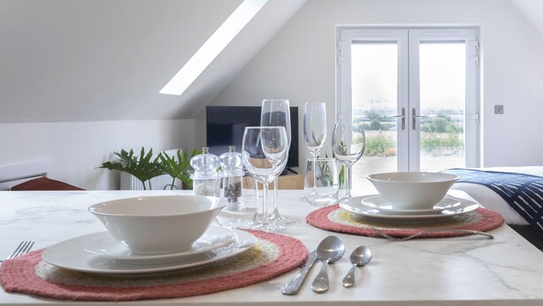 A dining table set with white plates, bowls, and cutlery, with a view of a balcony and a door in the background. - Beautiful Self Contained Annex in Toddington (Cheltenham)