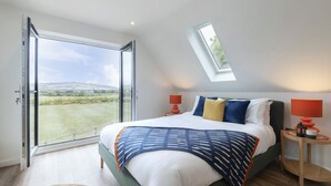 A bedroom with a large bed, two bedside tables, a skylight, and a view of a grassy field. - Beautiful Self Contained Annex in Toddington (Cheltenham)