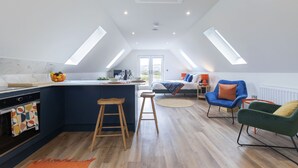 A modern kitchen with a central island, wooden stools, and a dining area with a sofa and chairs. - Beautiful Self Contained Annex in Toddington (Cheltenham)