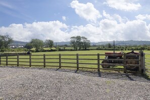 Ländliche Landschaft mit einem Schotterweg, Holzzaun und einem Traktor auf einem Feld.