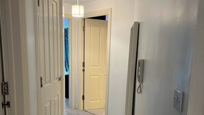 Een gang met vloerbedekking, witte muren en een deur naar een andere kamer.