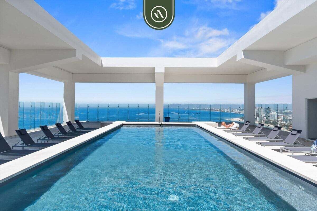 Una piscina infinita en la azotea con sillones reclinables y una vista despejada del horizonte de la ciudad.