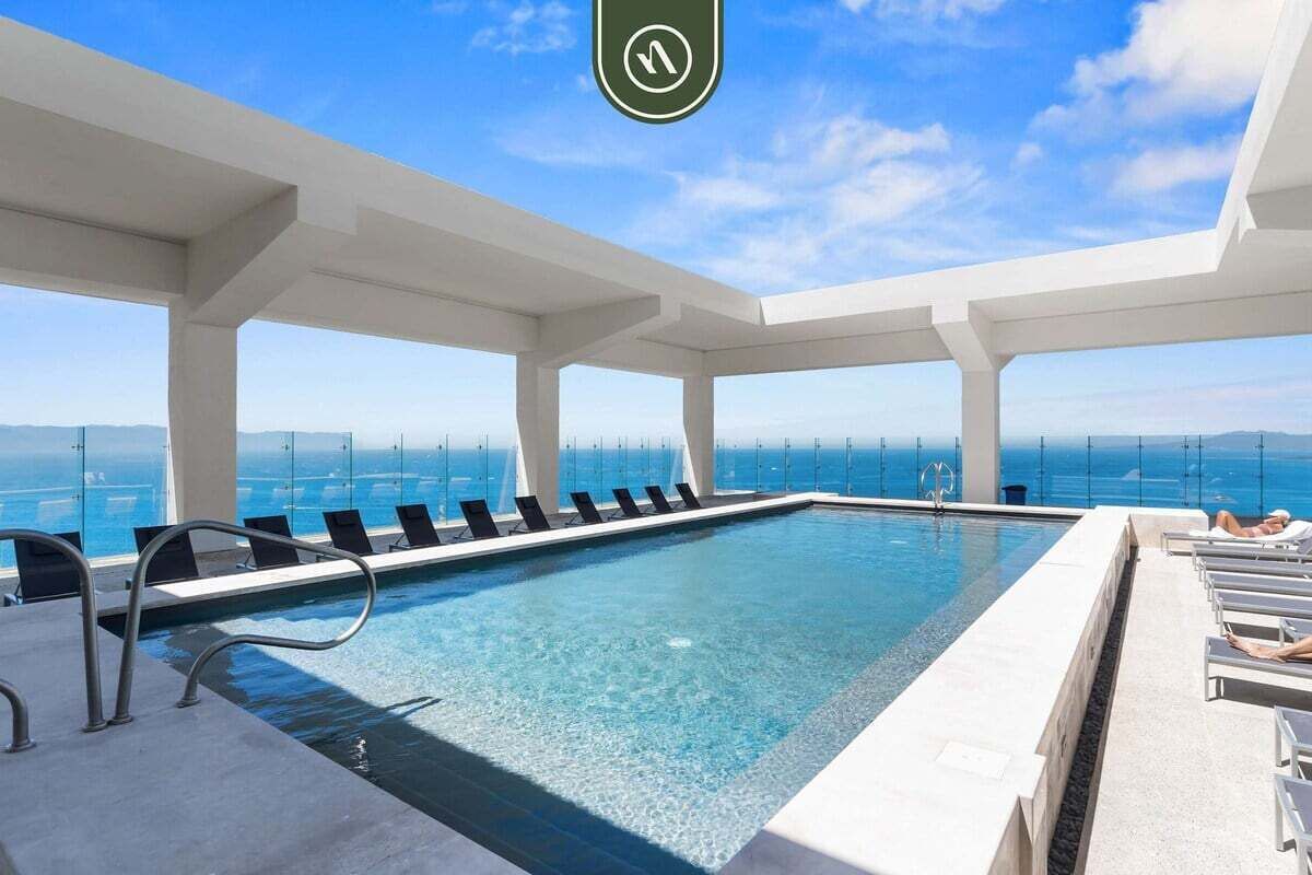 Una piscina infinita al terrat amb aigua blau turquí, envoltada de pilars blancs, i vistes a l'oceà.