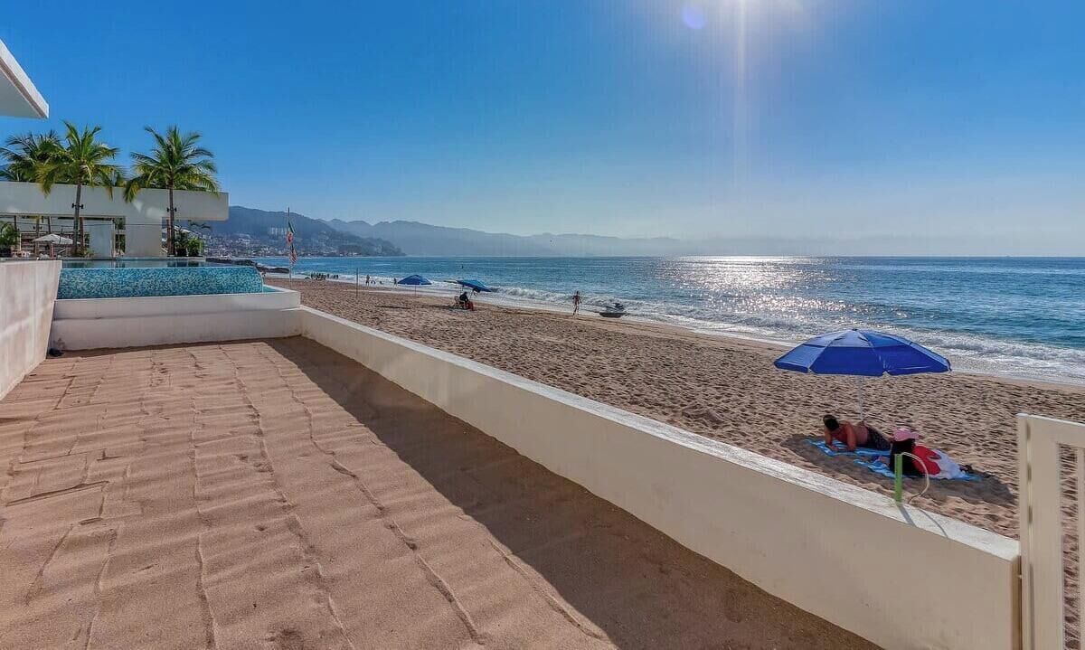 A beach view with a pool, umbrellas, and a clear sky.