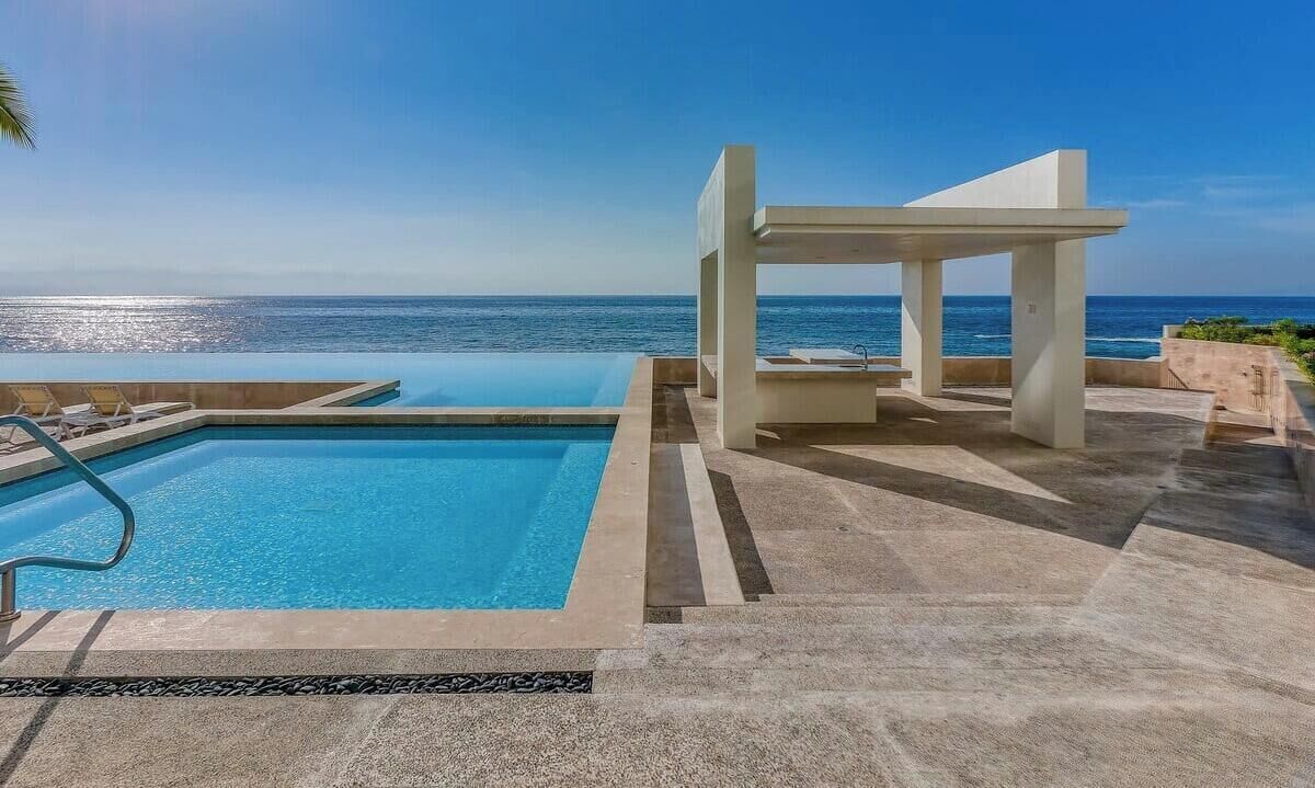 Ein Pool mit Blick auf den Ozean, eine überdachte Sitzgelegenheit und eine geflieste Terrasse.