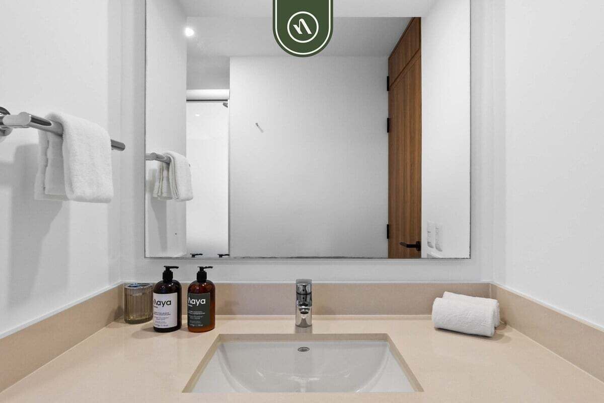 A bathroom with a large mirror, a sink, and two bottles of Naya soap.