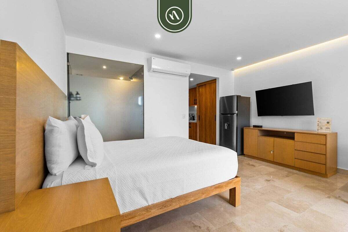 Moderni hotellihuone, jossa on sänky, televisio, vaatekaappi ja kylpyhuone, joka on näkyvissä lasiovesta.