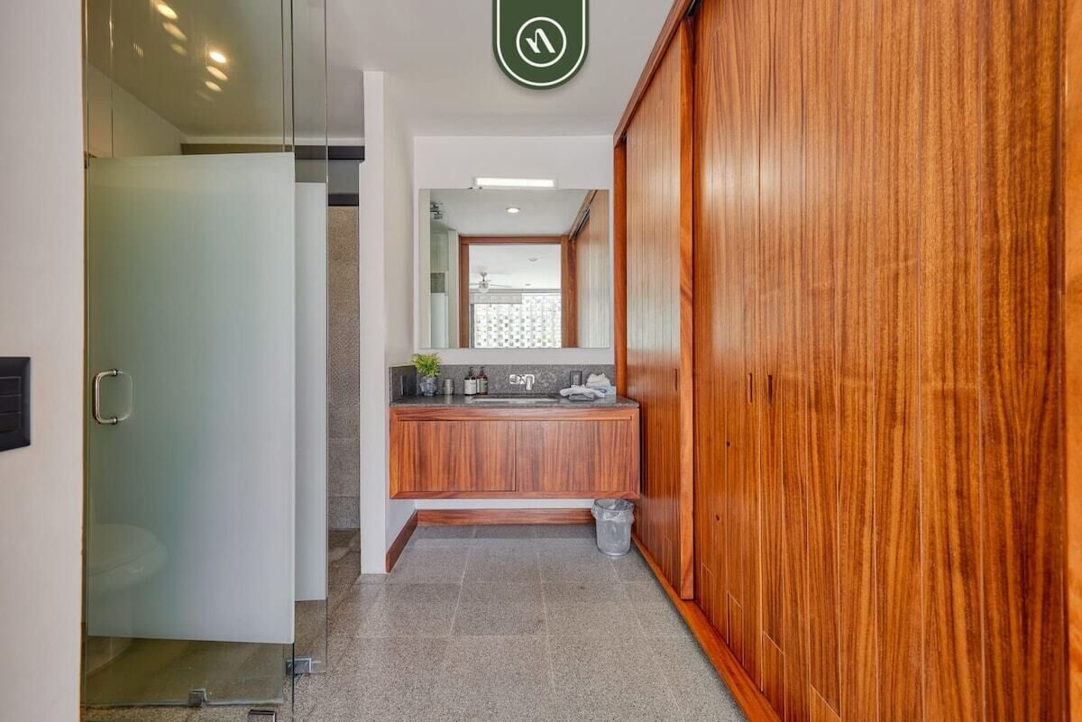 A hallway with a wooden wardrobe, a glass door leading to a bathroom, and a sink area with a mirror and countertop.