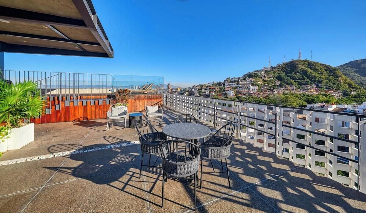 Una terraza en la azotea con mobiliario exterior, vistas a la ciudad y una valla de madera.