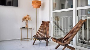 A room with two wooden chairs, a floor lamp, a small table with a vase, and a large window with a metal railing. - Amazing 1BR - Rooftop Pool in Versalles (Puerto Vallarta)