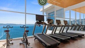 Un gimnasio con cintas de correr y bicicletas estáticas, amplias ventanas con vistas al océano.