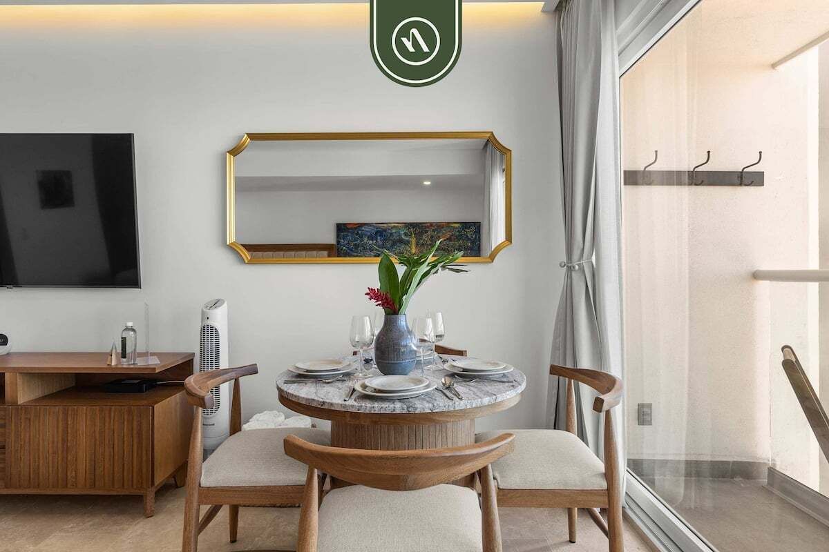 Un comedor con una mesa redonda, sillas, un florero con flores y un televisor en la pared.