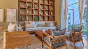 Una sala de estar con un sofá, dos sillas de madera, una mesa de centro y una estantería de madera llena de objetos decorativos.