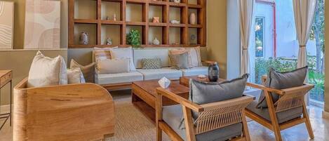 A living room with a sofa, two wooden chairs, a coffee table, and a wooden bookshelf filled with decorative items.