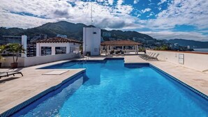 A rooftop pool with clear blue water, lounge chairs, and a view of mountains and a body of water. - Ocean View 2Br Condo-balcony-beach-pool VDS 111 (Puerto Vallarta)