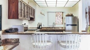 A kitchen with a granite countertop, stainless steel appliances, and a white backsplash. There are two white bar stools and a decorative vase with branches. - Ocean View 2Br Condo-balcony-beach-pool VDS 111 (Puerto Vallarta)