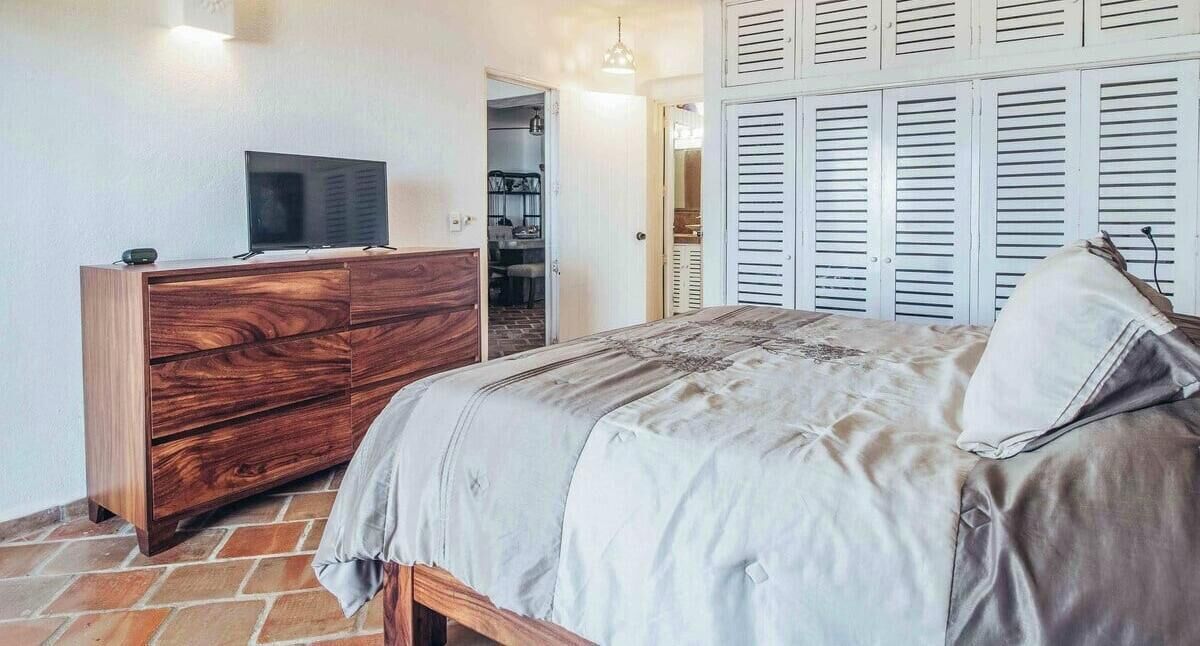 Ein Schlafzimmer mit einem Holzkleiderschrank, einem Bett mit gemustertem Bettbezug und einem Schrank mit weißen Klappläden.