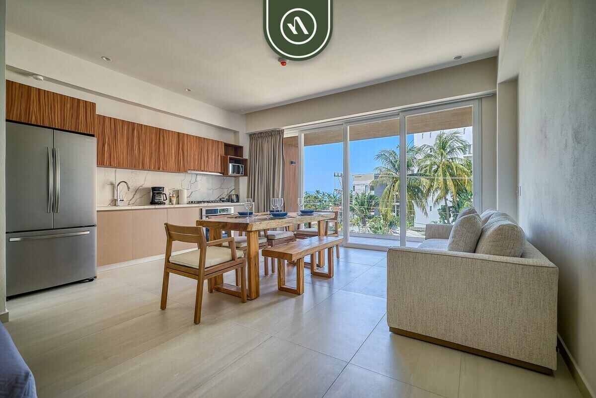 A modern kitchen with a dining area, a sofa, and a large sliding glass door to the outside.