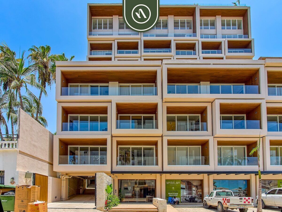 Un hotel de varios pisos con balcones, un restaurante a la vista y un estacionamiento.