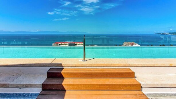 Vista chiara di una piscina con un pontile in legno in primo piano e una lontana veduta del paesaggio costiero.