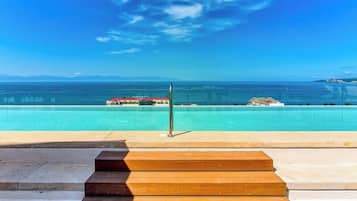 A clear view of a swimming pool with a wooden deck in the foreground and a distant view of a coastal landscape.