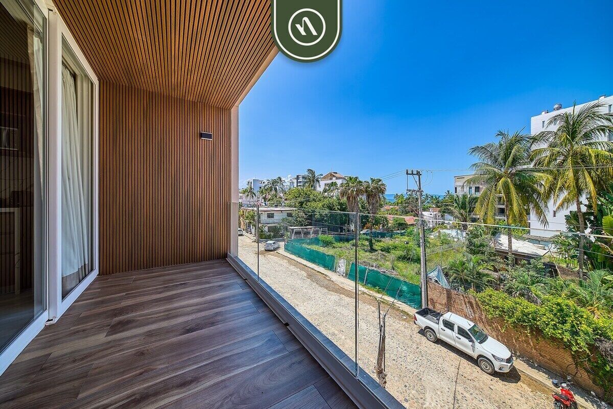 Un balcón con vistas a una carretera y edificios, techo de madera y puerta de cristal.