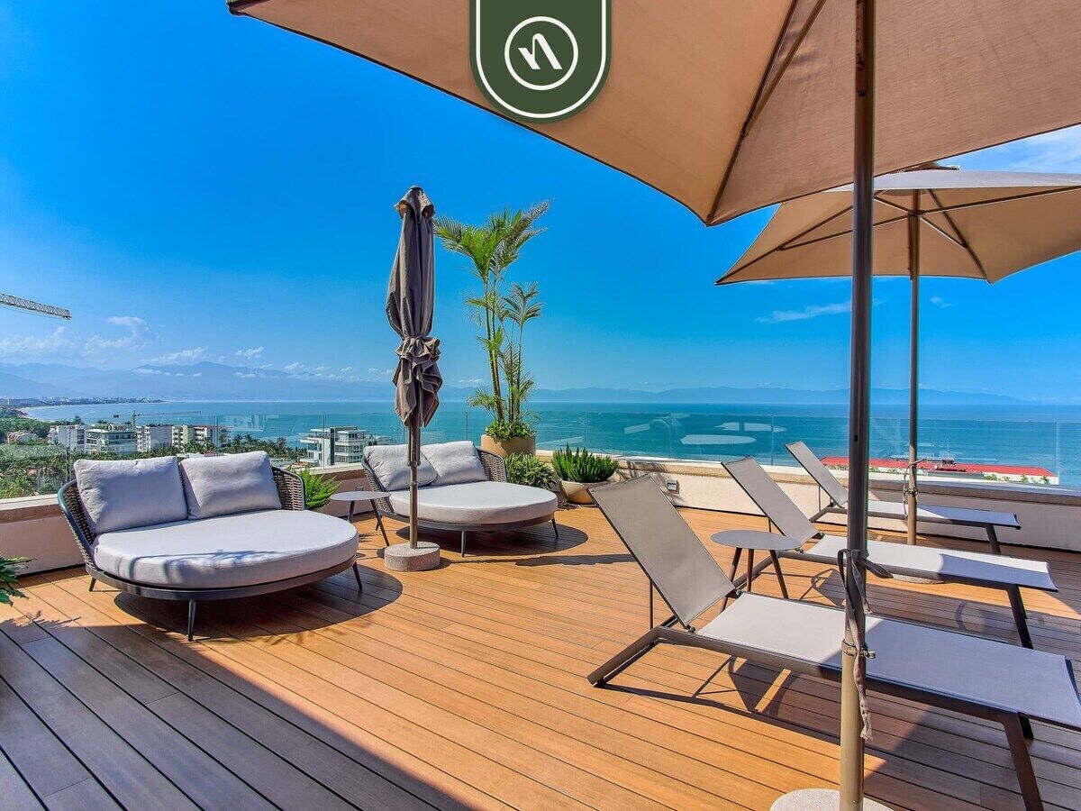 A wooden deck with lounge chairs and a large umbrella, overlooking a coastal view.