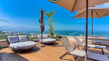 A wooden deck with lounge chairs and a large umbrella, overlooking a coastal view.