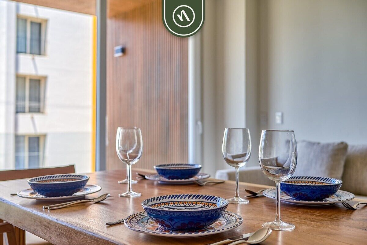 A dining table with blue patterned bowls and wine glasses, a wooden chair, and a view of a building outside.