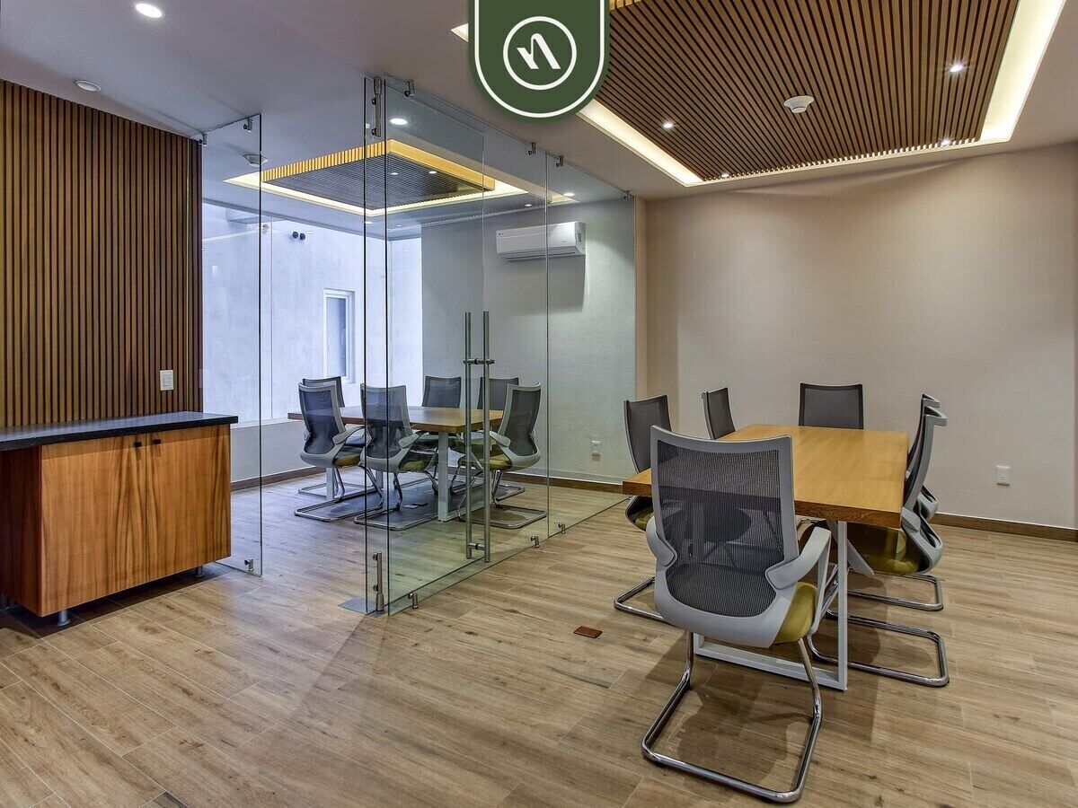 Un ufficio moderno con scrivania di accoglienza in legno, pareti in vetro, un tavolo da conferenza con sedie e un soffitto con illuminazione a incasso.