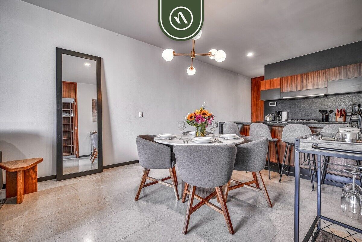 A modern kitchen with a dining area, a large mirror, and a ceiling light fixture.