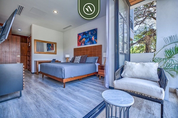 A modern bedroom with a bed, bedside table, chair, and a view of the outdoors. - New 2BR Condo in Zona Romantica - Rooftop Pool (Puerto Vallarta)