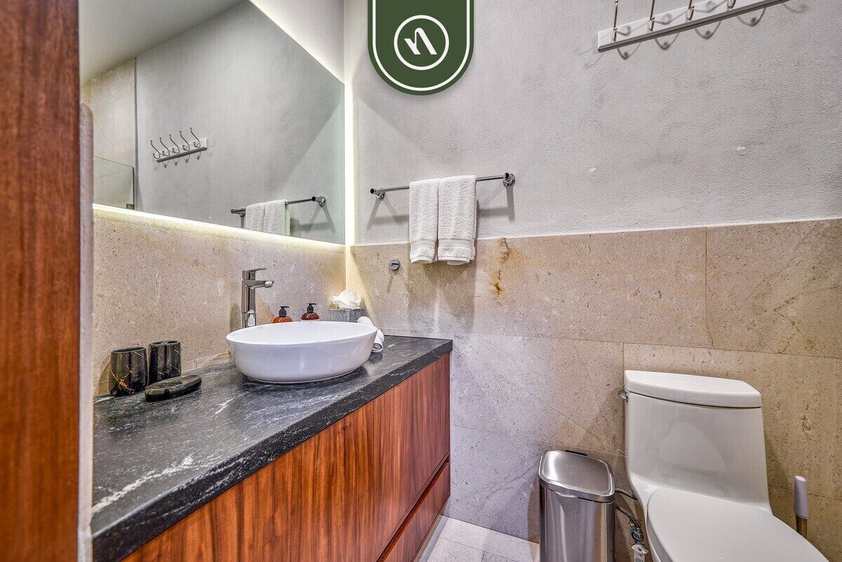 A bathroom with a white sink, wooden vanity, a towel rack, a toilet, and a trash bin.