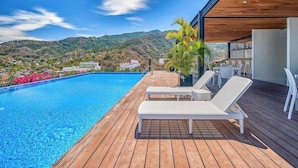 A wooden deck with a pool, lounge chairs, and a view of hills. - New 2BR Condo in Zona Romantica - Rooftop Pool (Puerto Vallarta)