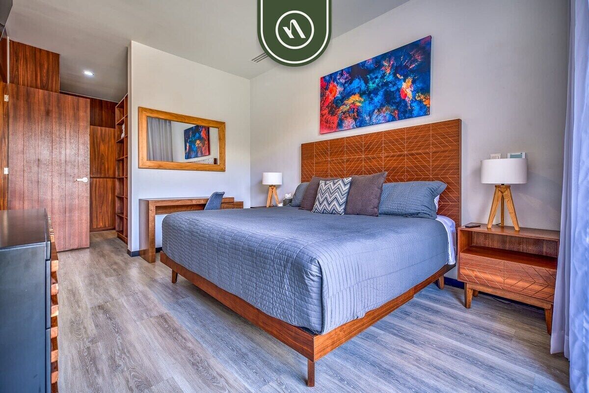 A modern hotel room with a large bed, wooden headboard, a desk, and a wardrobe.