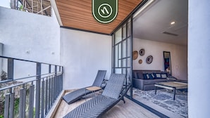 A balcony with two lounge chairs, a sofa, and a coffee table inside a modern room with large windows and a wooden ceiling. - New 2BR Condo in Zona Romantica - Rooftop Pool (Puerto Vallarta)