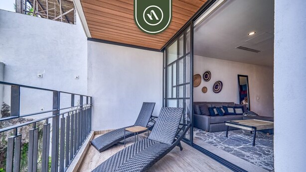 Un balcon avec deux fauteuils de relaxation, un canapé et une table basse, situé dans une pièce moderne dotée de grandes fenêtres et d’un plafond en bois.