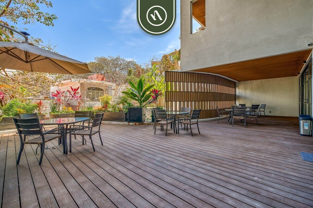 A wooden deck with outdoor seating, surrounded by plants and a building with a modern design.