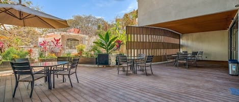 A wooden deck with outdoor seating, surrounded by plants and a building with a modern design.
