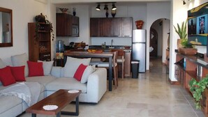 Una sala de estar con sofá, una mesa de centro y una zona de cocina con armarios y un refrigerador.
