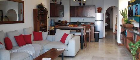 A living room with a sofa, a coffee table, and a kitchen area with cabinets and a refrigerator.