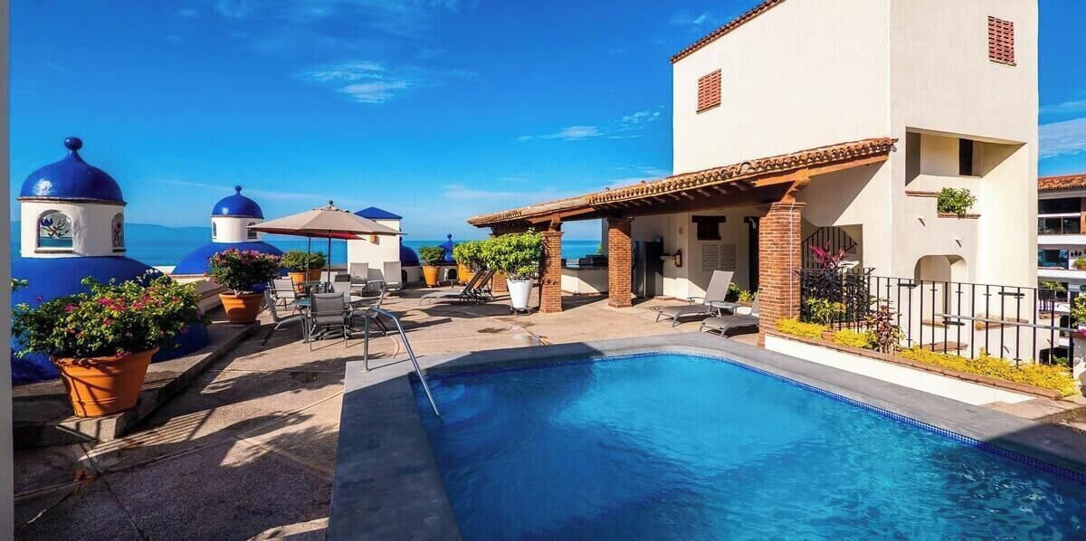 A pool area with a clear view of the sea, a building with a tiled roof, and a structure with blue domes.