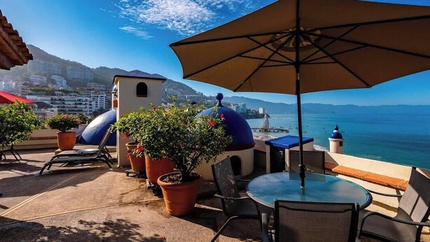 Una terraza con mobiliario exterior, plantas en macetas y vista al mar.