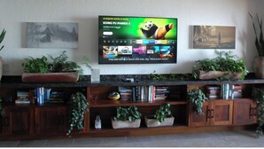 Una sala de estar con un televisor de pantalla plana montado en la pared, rodeada de estanterías y plantas en macetas.