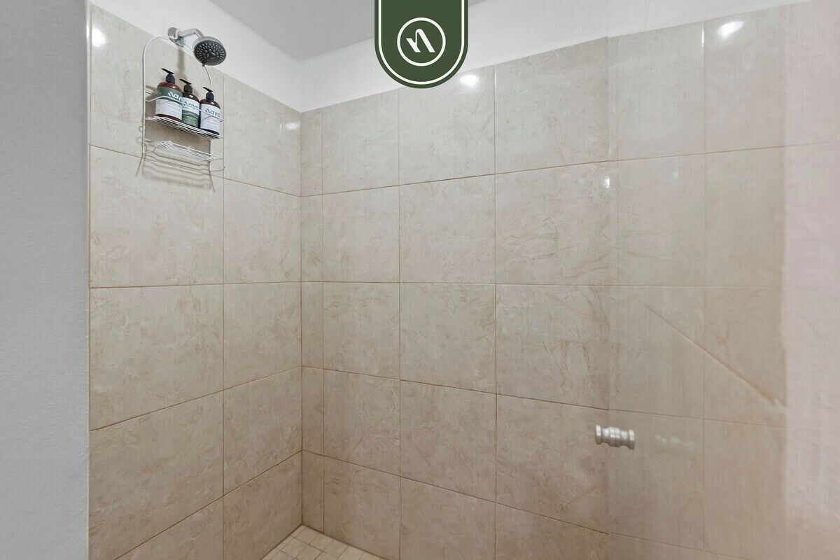 A shower area with beige tiles, a showerhead, and a shelf with toiletries.