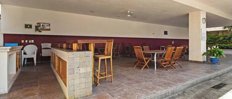 A covered outdoor seating area with a counter, chairs, and tables.