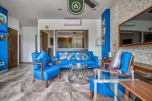 Un salon moderne avec un canapé bleu, des fauteuils assortis, une table basse en verre et un grand miroir.