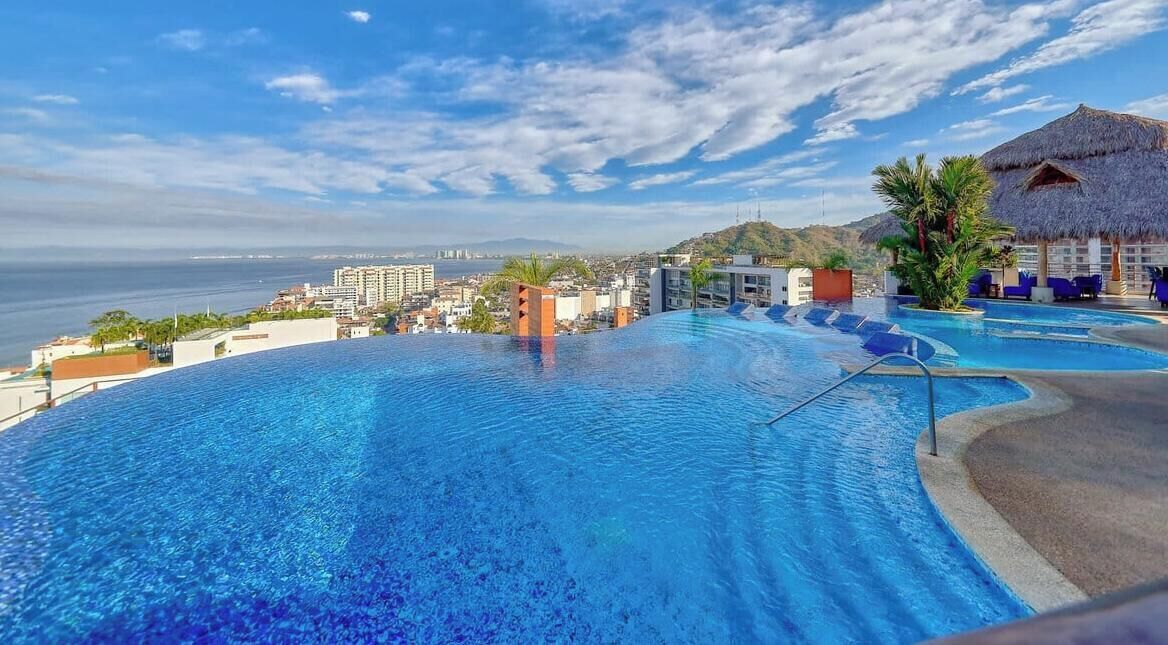 Una amplia piscina al aire libre con vistas al océano y edificios al fondo.