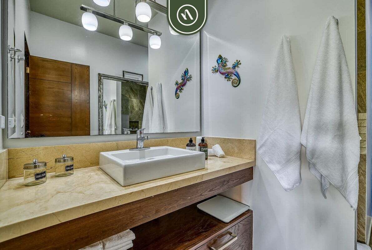 A bathroom with a large mirror, a white sink, and decorative wall art.